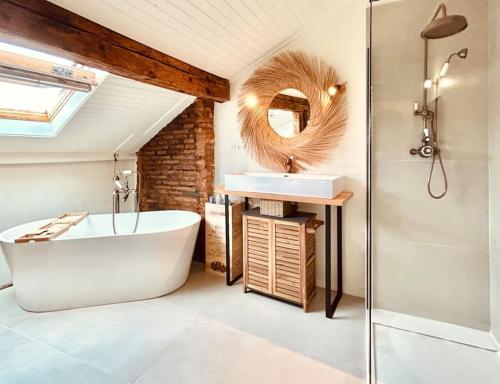 La salle de bains est pourvue d'une baignoire, d'un lavabo et d'un miroir. dans l'établissement Les Puits Clos : magnifique T2 sous les toits, à Toulouse