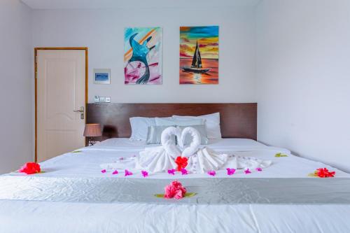 Una cama blanca con dos toallas de cisne y flores. en Violet Inn Hotel, en Dharavandhoo