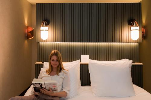 a woman sitting on a bed reading a book at Boutique Hotel Helder I Kloeg Collection in Renesse
