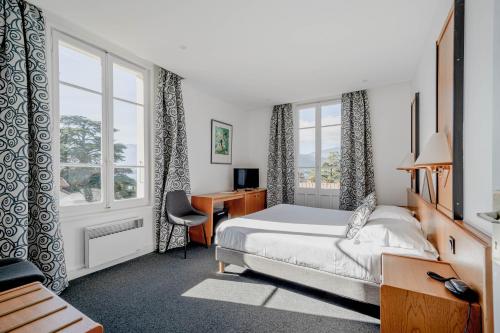 a bedroom with a bed and a desk and window at Hotel du Lac in Talloires
