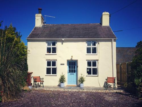 a white house with two chairs and a blue door at Gorgeous Cottage Near the Sea. Dog Friendly. in Ederyn