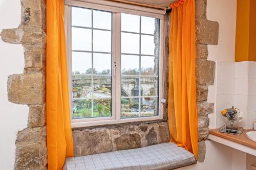 a window with orange curtains in a bathroom at Bridge End Mill by Guestz in Settle