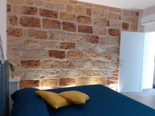 - un mur en briques avec un lit bleu et des oreillers jaunes dans l'établissement Camere Stella del Sud Makari, à Macari