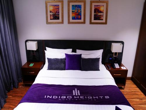 1 dormitorio con 1 cama grande con almohadas moradas en Indigo Heights Hotel & Suites en Lahore