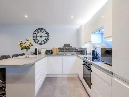 a kitchen with white cabinets and a clock on the wall at THE HIDEOUT, a Detached Lodge, Hot Tub, Heating, WiFi & Parking in Long Bredy