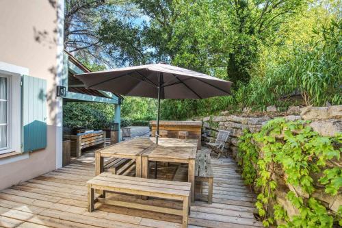 une table en bois avec un parasol et des bancs sur une terrasse dans l'établissement Villa des Roses - Welkeys, à Grimaud