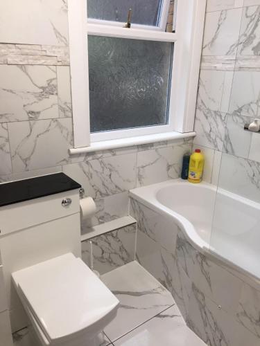 Devons Unique Short Stay في لندن: حمام أبيض مع حوض ومرحاض ونافذة