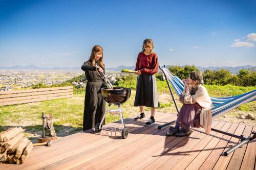 倉敷的住宿－OKAYAMA GLAMPING SORANIA - Vacation STAY 73195v，一群三名妇女坐在吊床上,并使用烤架