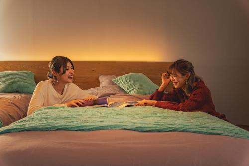 dos mujeres sentadas en una cama leyendo un libro en OKAYAMA GLAMPING SORANIA - Vacation STAY 19628v en Kurashiki
