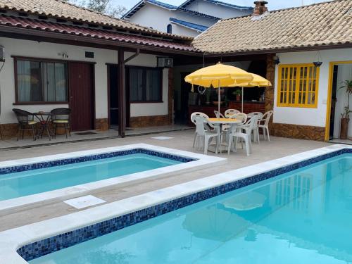 a swimming pool with a table and an umbrella next to a house at Pousada Fazendinha Unamar in Cabo Frio