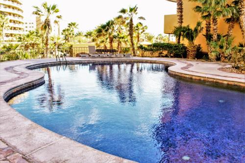 a swimming pool with palm trees and a building at Bella Sirena Beauty 201-C - Stunning Views & Beachfront Bliss in Puerto Peñasco