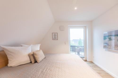 - une chambre blanche avec un grand lit et des oreillers blancs dans l'établissement Getidenhus Lütje, à Sankt Peter-Ording
