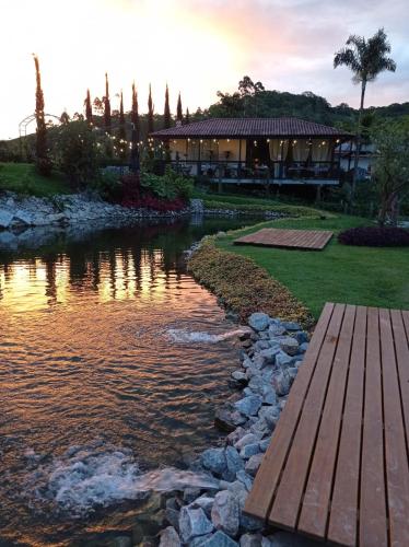 a river with a wooden bridge in front of a house at Pousada e Restaurante Casa Cida e Evandro in Gaspar
