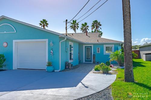 a blue house with a driveway and palm trees at Relaxing Beach Home with Fire Pit and Private Fenced Yard STEPS from the Sand! in New Smyrna Beach