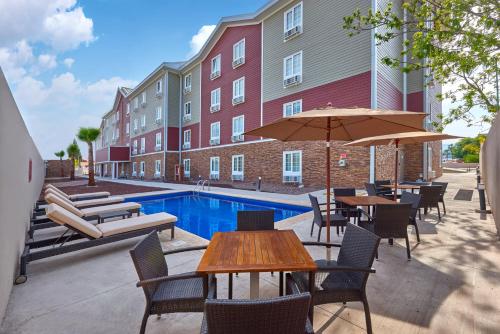 eine Terrasse mit Tischen und Stühlen und einem Pool in der Unterkunft Extended Suites Chihuahua La Juventud in Chihuahua