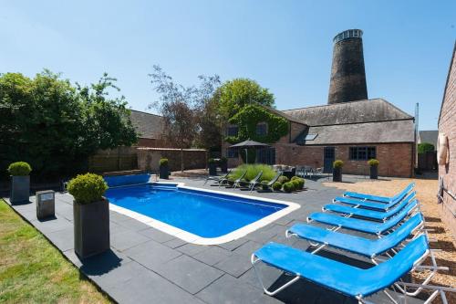 a swimming pool with lounge chairs next to a building at The Old Mill, 7 storey,, dog friendly outdoor pool & bbq in Stoke Ferry