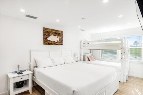 a white bedroom with a bunk bed and a window at A Wave From it All in Key Colony Beach
