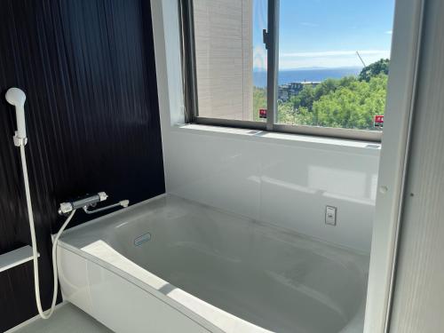 baño con bañera blanca y ventana en Ｖｉｌｌａ・Ｃｈａｒｍｅ, en Motobu