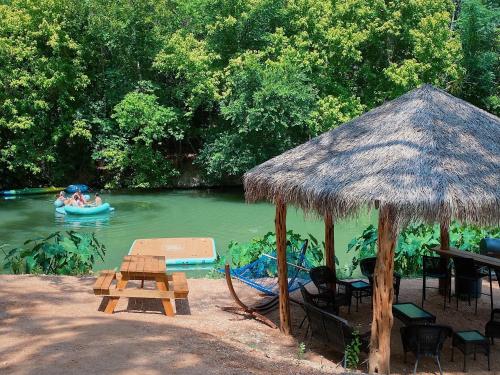 a picnic table and a hut with people in a boat in the water at Son's Rio Cibolo Glamping Cabin #G Brand New Creek-front Cabins with SO Many Amenities! in Marion