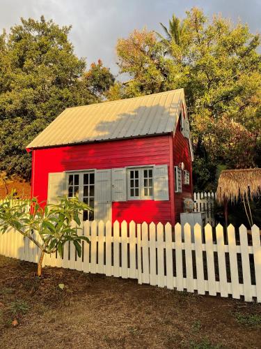 a red house behind a white fence at La Petite Kaz Dans la Savane in Fleurimont