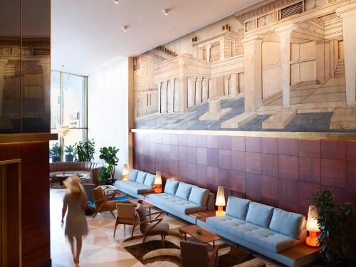 a woman walking through a lobby with blue couches at Brown Acropol, a member of Brown Hotels in Athens