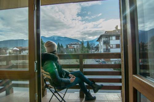 un hombre sentado en una silla en un balcón con vistas a una ventana en Banderitsa Apartments with kitchen & BBQ, en Bansko