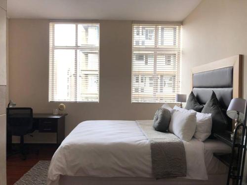 a bedroom with a bed and a desk and two windows at Seventh Heaven in Johannesburg