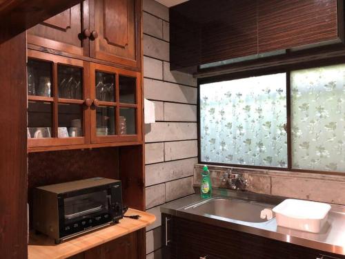 a kitchen with a microwave and a sink and a window at 那須町湯本の那須御用邸近くのログハウス in Nasu-yumoto