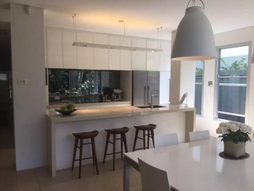 uma cozinha com armários brancos e bancos de bar em Modern Queens Park Home near Bondi Junction, Bondi Beach & City em Sydney