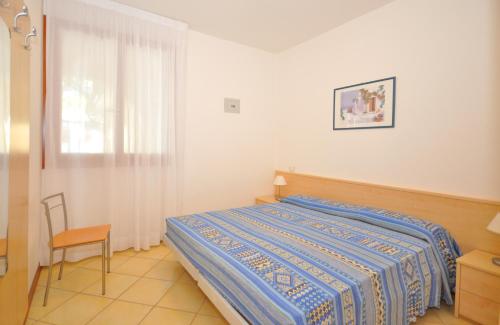 a bedroom with a bed and a chair and a window at Villaggio Orchidea in Bibione
