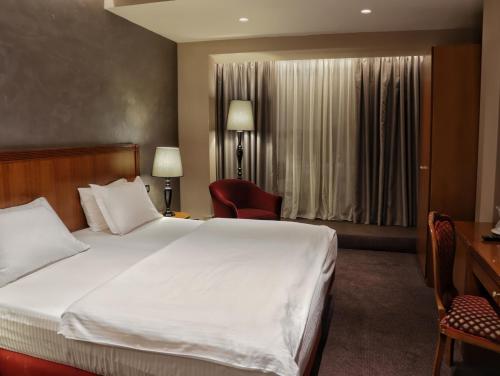 a hotel room with a large white bed and a desk at Mondial Hotel in Tirana