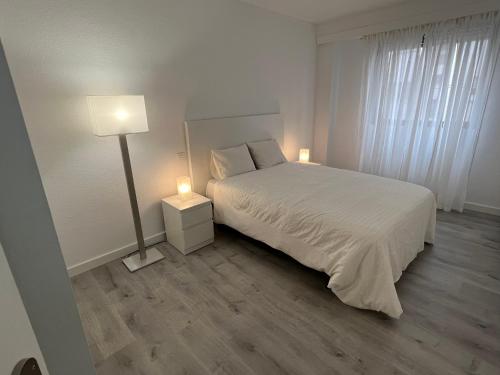 a white bedroom with a bed and a lamp at Apartamento 1 dormitorio cerca hospitales in Zaragoza
