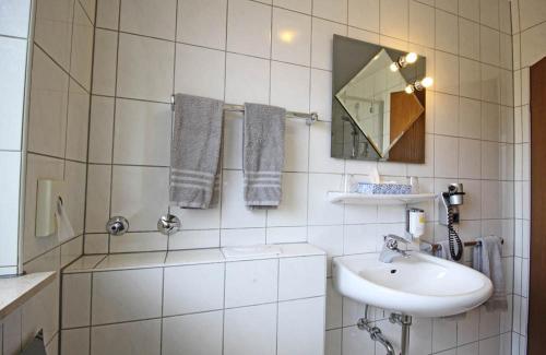 a white tiled bathroom with a sink and a mirror at Hotel Lindenkrug in Gütersloh