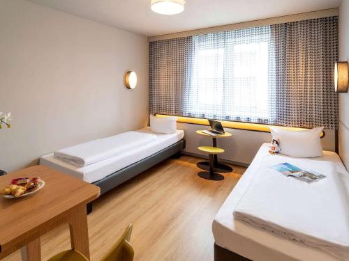 um quarto de hotel com duas camas e uma mesa e uma janela em Aparthotel Adagio Access Freiburg em Friburgo em Brisgóvia