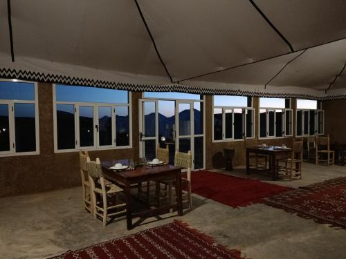 a dining room with tables and chairs and windows at Sun Bivouac Chegaga in El Gouera