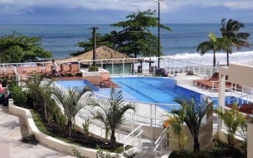 een zwembad van het resort met de oceaan op de achtergrond bij Lindo Apartamento de Frente para o mar in Caraguatatuba