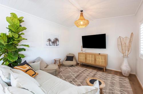 a living room with a white couch and a flat screen tv at Sea Breeze Cottage - oceanstays in Yamba