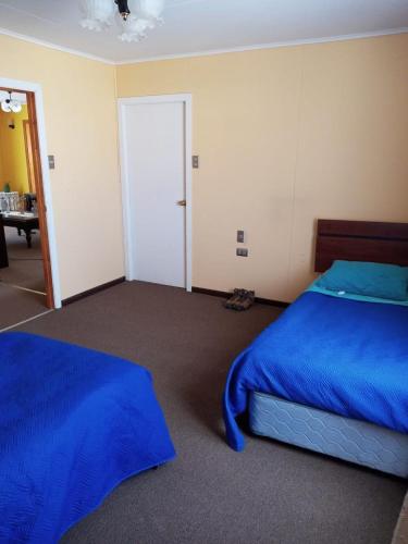 a bedroom with two beds with blue sheets and a door at HOWENH in Porvenir