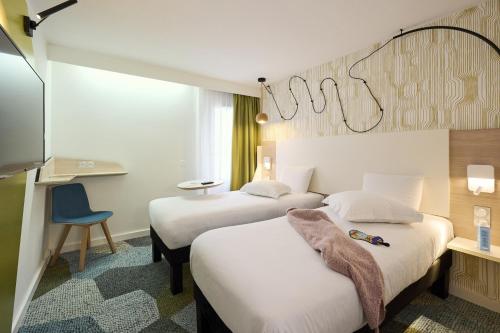 a hotel room with two beds and a chair at ibis Styles Bordeaux Begles in Bègles