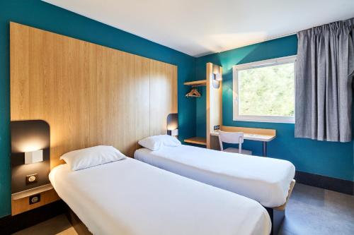 2 camas en una habitación con paredes azules y ventana en B&B HOTEL Evry Lisses 2, en Lisses