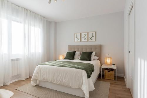 a white bedroom with a large bed with green pillows at El Prau de Mito in Cangas de Onís