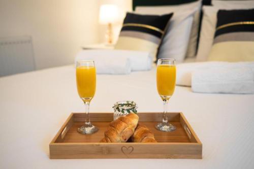 two glasses of orange juice and bread on a tray on a bed at Milverton Hotel in Manchester