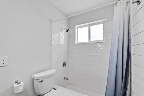 a white bathroom with a toilet and a window at Spacious Modern Home 5BR Heated Pool, 9mn to Beach in Miami