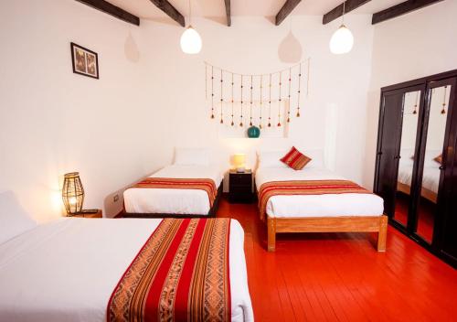 two beds in a room with white walls and wood floors at Hotel Kuska Home in Cusco