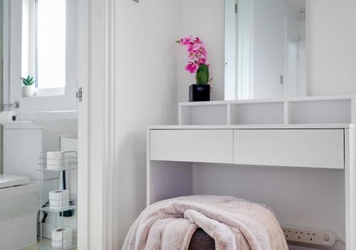 uma casa de banho branca com um toucador branco e um vaso de flores em Lovely 4 Bedroom London Home with Free Parking, Garden, WiFi By Roost Accommodation em Kingston upon Thames