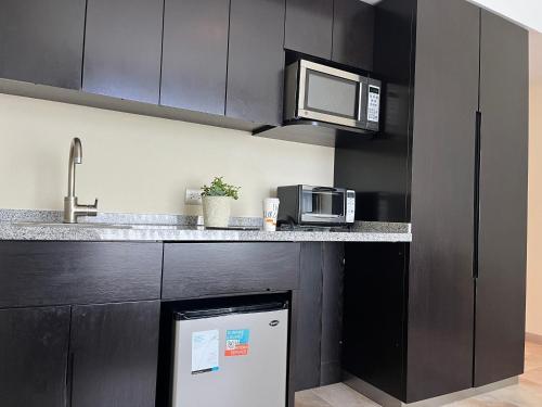 a kitchen with black cabinets and a microwave and a refrigerator at Stadia Suites Mexico City Santa Fe in Mexico City