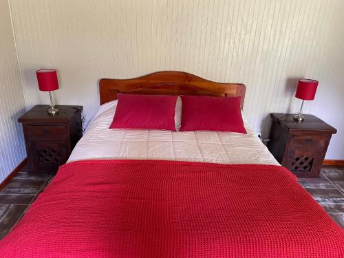 a bed with two red pillows and two night stands at Campito Refugio in San José de Maipo