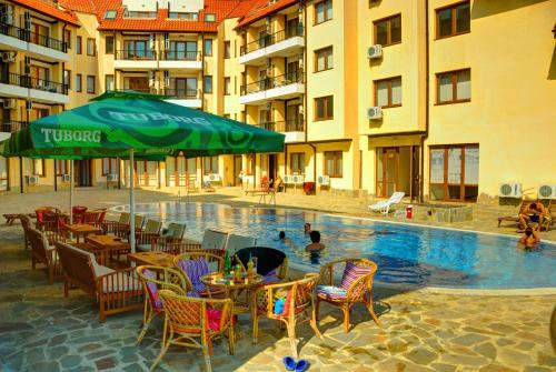 a pool with tables and chairs and a green umbrella at Oasis Beach Apartments Kamchia in Kamchia