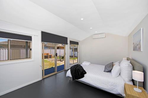 a white bedroom with a bed and large windows at Large Cottage Near Ettalong Centre in Ettalong Beach