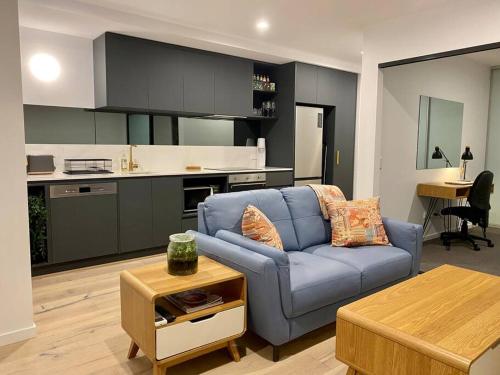 a living room with a blue couch and a kitchen at Central Canberra City apartment with study and full amenities including parking in Canberra